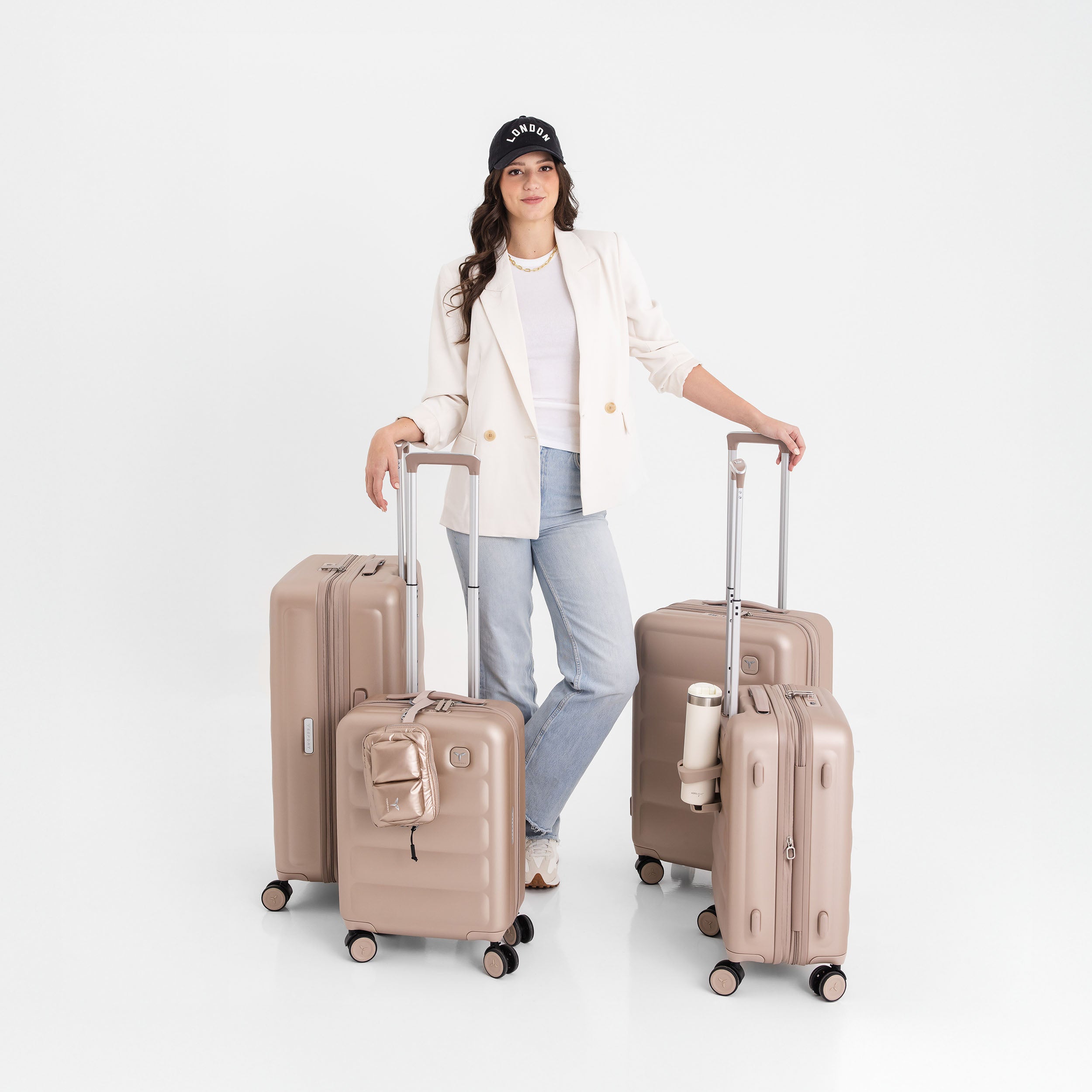 Woman standing with three champagne Tesport Cloud Collection suitcases on a white background