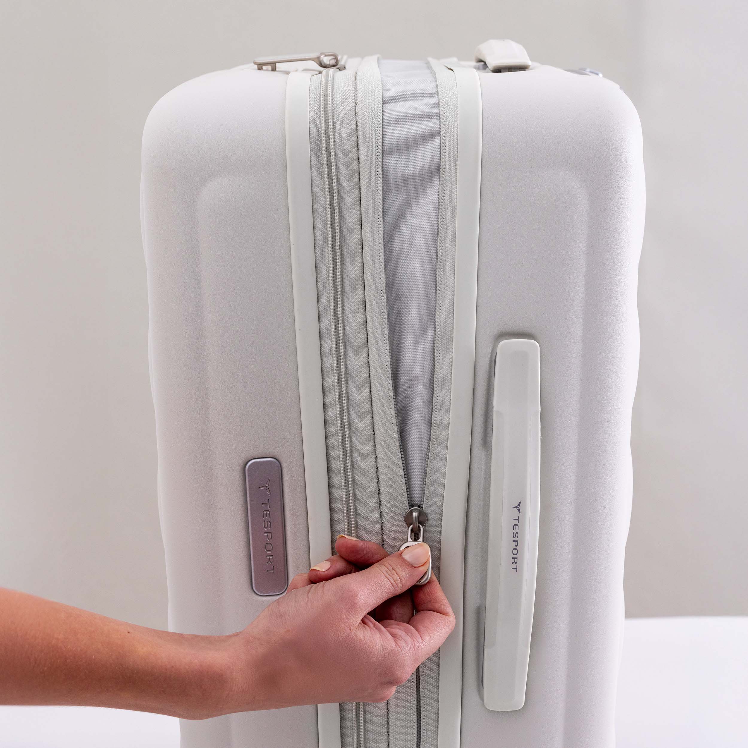 Tesport Cloud Collection White suitcase with a hand opening the zipper on a light gray background