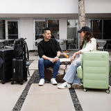 Two people sitting on a stone bench with suitcases around them with Tesport black and apple green Cloud Collection pieces.