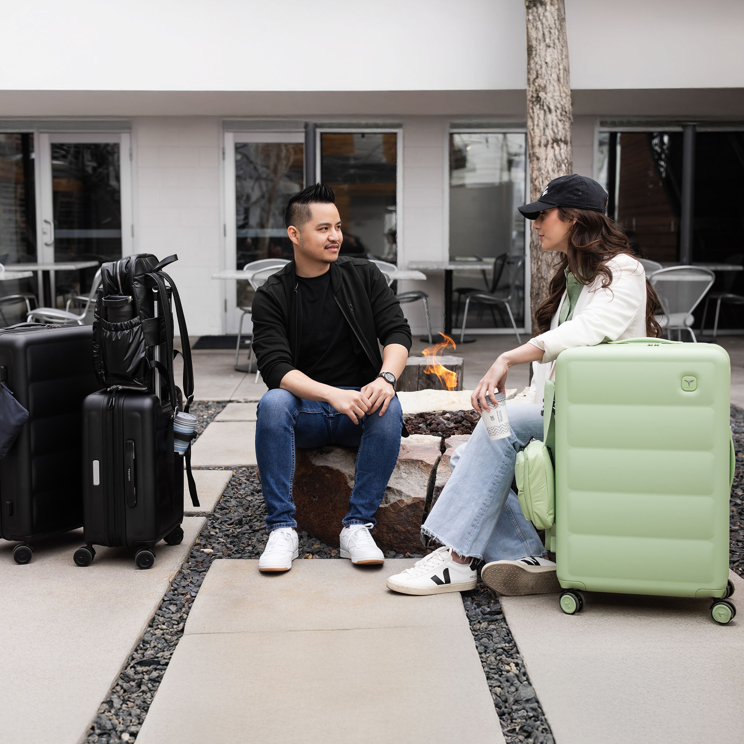 Two people sitting on a stone bench with suitcases around them with Tesport black and apple green Cloud Collection pieces.