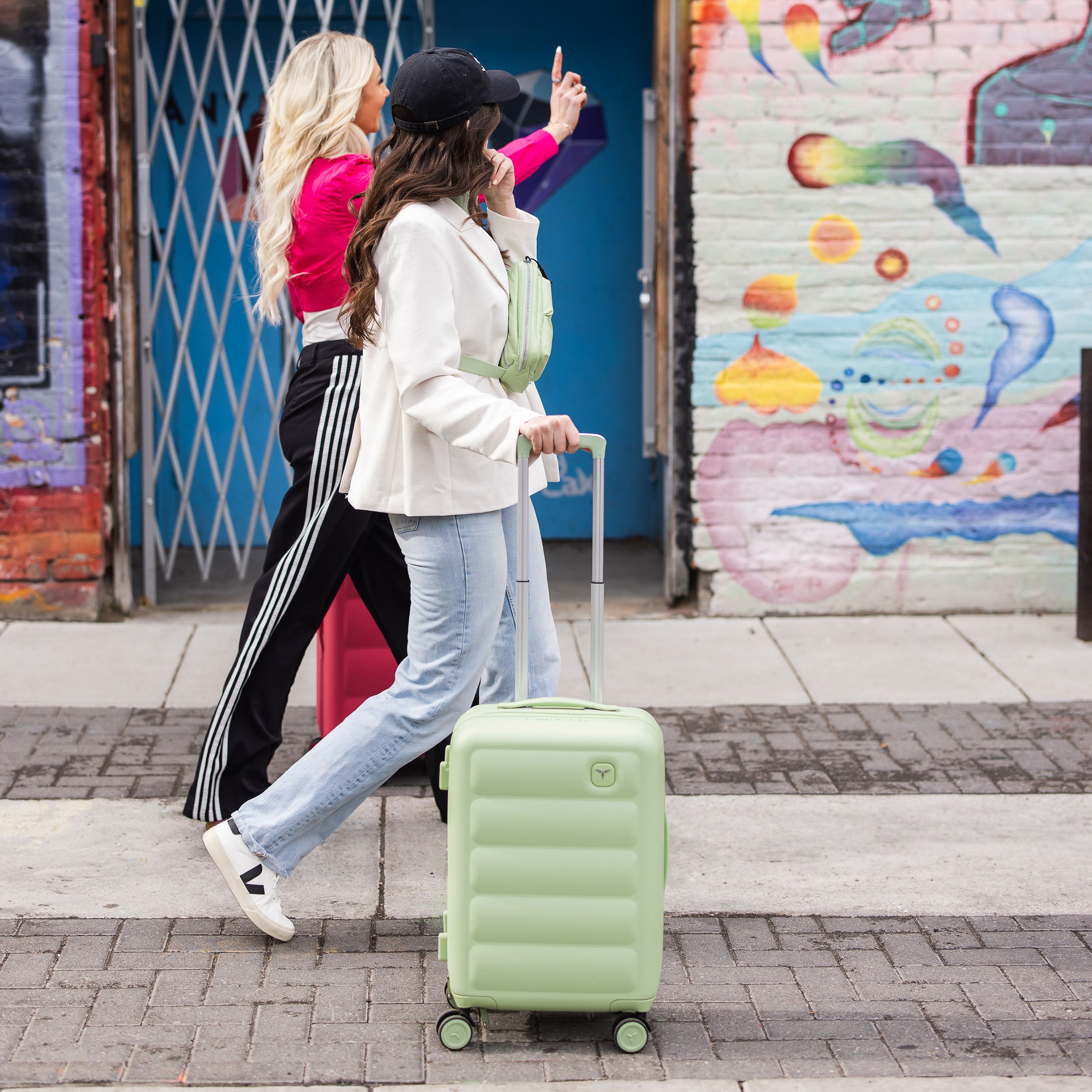 Two people walking with a Tesport Cloud Collection apple green suitcase against a colorful mural background