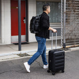 Man with a Tesport Cloud Collection black backpack and suitcase walking outside a building.