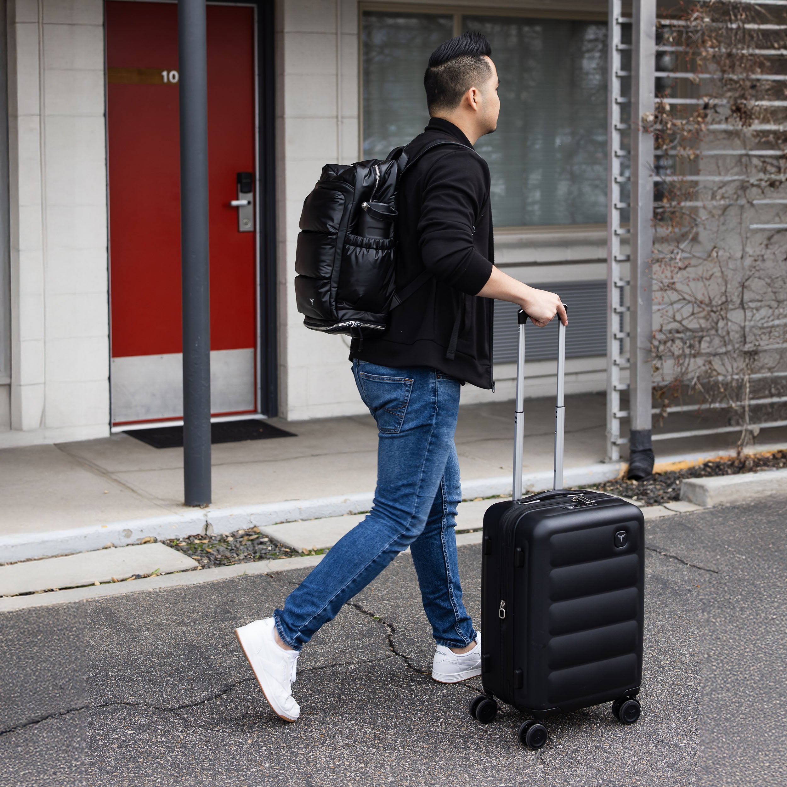 Man with a Tesport Cloud Collection black backpack and suitcase walking outside a building.